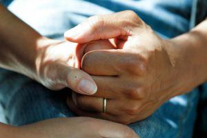 Close-up of two hands clasped together, one showing a wedding ring, on a blurred background